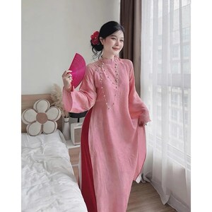 May include: A pink traditional dress with long sleeves and a high collar. The dress has a split on the side, revealing a red underlayer. A pink fan is held in the hand. The dress is adorned with delicate embroidery and a pearl necklace.
