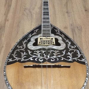 Peut inclure: Un bouzouki grec traditionnel avec un motif floral noir et blanc sur le corps. L'instrument a un corps en bois et une rosace en métal argenté.