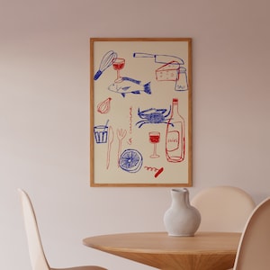 May include: A framed print with a white background and blue and red illustrations of various kitchen items, including a fish, a crab, a bottle of wine, a glass of wine, a knife, a whisk, a lemon, a fork, a spoon, a glass, a salt shaker, and the text "la cuisine" and "olive". The print is hanging on a light pink wall above a wooden table with two light brown chairs.