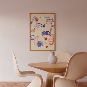 May include: A framed illustration of a kitchen scene with a blue and red color scheme. The illustration includes a fish, a crab, a wine bottle, a glass of wine, a lemon, a corkscrew, a knife, a whisk, a fork, a spoon, a salt shaker, and a glass. The illustration is on a cream background and is framed in a light wood frame. The frame is hanging on a white wall. There are two white chairs and a wooden table in the foreground.