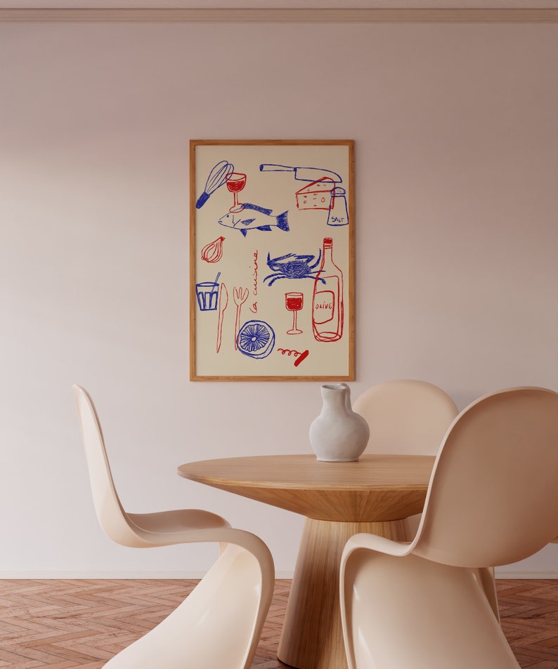 May include: A framed illustration of a kitchen scene with a blue and red color scheme. The illustration includes a fish, a crab, a wine bottle, a glass of wine, a lemon, a corkscrew, a knife, a whisk, a fork, a spoon, a salt shaker, and a glass. The illustration is on a cream background and is framed in a light wood frame. The frame is hanging on a white wall. There are two white chairs and a wooden table in the foreground.