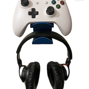 May include: A white Xbox controller with a blue stand and black headphones hanging from the stand.