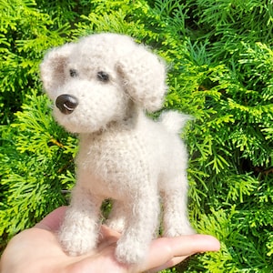 Puede incluir: Un juguete de perro de crochet blanco con textura esponjosa. El juguete está de pie sobre una mano.