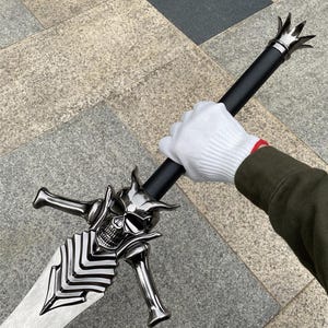 以下が含まれることがあります： メタリックシルバーの刃と複雑なヒルトデザインが特徴の剣。クロスガードは角のような突起と骨の形をしたクィロンを持つ様式化された頭蓋骨の形をしています。ハンドルは黒で、端には王冠の形をしたポメルが付いています。