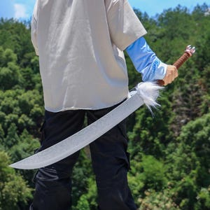 May include: A curved sword featuring a long, light-colored blade with intricate etched patterns, a white faux fur accent at the hilt, and a brown wrapped handle with a silver-toned pommel, held in a downward position against a natural backdrop.