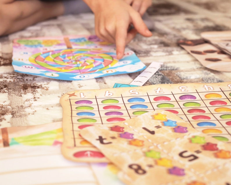 May include: A colorful game board with a spiral design and numbers 1 through 5. There are also several smaller game boards with jelly bean images and math equations.