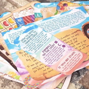 May include: A stack of colorful game cards with whimsical illustrations and text. The cards feature a candy theme and include instructions for a game or activity. The text on the cards includes phrases like "How to Open the Portal to Candylleria?" and "Symbols on the Lock?"