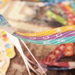 May include: A close-up of a colorful, multi-layered ribbon with the words "What We Do" printed on the top layer. The ribbon is made of three different colors: orange, purple, and blue. Each color has a wavy pattern and white letters.