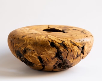 May include: A large, rustic wooden bowl with a natural, organic shape and a deep, round opening. The bowl is made from a single piece of wood with a rich brown color and a textured surface.