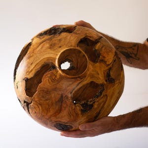 Man's hands holding a Large wood vase, organic modern shape with bark inclusions and live-edge openings.