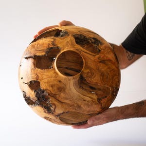 Man's hands holding a Turned olive wood vessel, hollow form with natural voids, organic modern style.