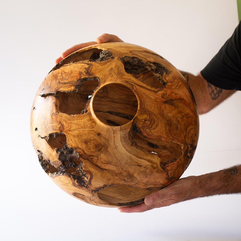 Man's hands holding a Turned olive wood vessel, hollow form with natural voids, organic modern style.