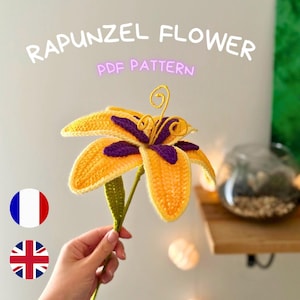 May include: A crocheted yellow and purple flower with the text "RAPUNZEL FLOWER PDF PATTERN". The flower has a green stem and is held by a person. The flower petals are yellow with purple accents.