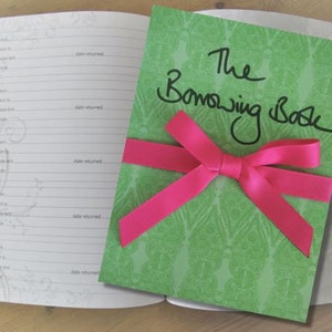 May include: A green book with a pink bow and the words "The Borrowing Book" written in black marker.