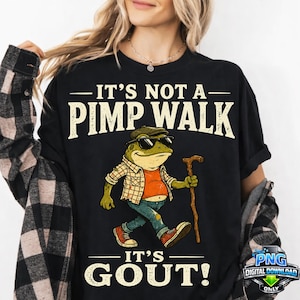 Może przedstawiać: Czarny t-shirt z grafiką zielonej żaby w koszuli w kratę, dżinsach, trampkach, czapce i okularach przeciwsłonecznych, trzymającej drewnianą laskę. Napis głosi IT'S NOT A PIMP WALK IT'S GOUT! wykonany jasną, postarzaną czcionką o wyraźnym kroju.