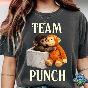 May include: Dark grey t-shirt with the words "TEAM PUNCH" above and below an illustration of two cartoon monkeys. One monkey is inside a grey block, and the other is hugging it. The image has a digital download logo.