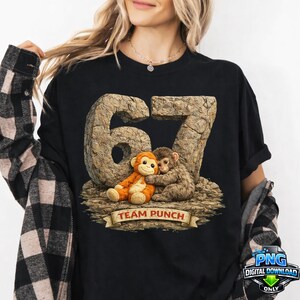 Op de afbeelding: Zwart T-shirt met een afbeelding van twee knuffelende apen, het nummer 67 in een steenachtige textuur. De tekst "TEAM PUNCH" staat op een banner. Het shirt heeft een ronde hals en korte mouwen. Digitaal download PNG-logo.