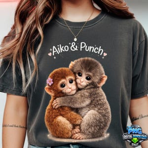 May include: Dark gray t-shirt featuring a graphic of two hugging monkeys with the text "Aiko & Punch". One monkey is brown with a pink flower, the other is gray. The design includes hearts and stars.