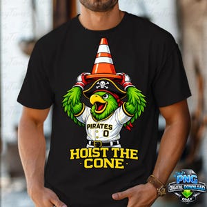 May include: Black t-shirt featuring a cartoon parrot wearing a pirate hat and holding an orange traffic cone. The parrot is wearing a baseball jersey that says "Pirates" and "0". The text "HOIST THE CONE" is below the parrot.