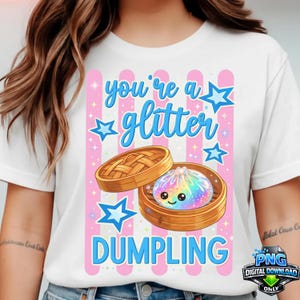 Puede incluir: Camiseta blanca con un gráfico que presenta una bola de masa sonriente de color arcoíris en una vaporera de bambú. El diseño incluye el texto "you're a glitter DUMPLING" en azul, con rayas rosas y estrellas.