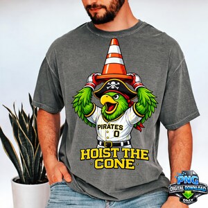 May include: Gray t-shirt featuring a cartoon parrot wearing a pirate hat and a baseball jersey with the text "Pirates 0". The parrot is holding an orange traffic cone. The text "HOIST THE CONE" is below the parrot.