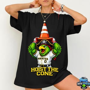 May include: Black t-shirt featuring a cartoon parrot wearing a pirate hat and a traffic cone. The parrot is wearing a baseball jersey with the word "Pirates" and the number "0". The text "HOIST THE CONE" is printed below the parrot.