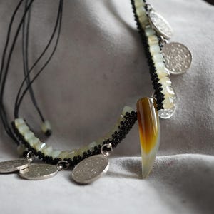 Könnte beinhalten: Eine mehrsträngige Halskette mit weißen und schwarzen Perlen, silbernen Anhängern und einem Anhänger aus braunem und weißem Achat.