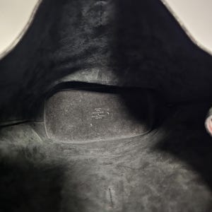 以下が含まれることがあります： 黒い革のトートバッグの内側。バッグは黒い布地で裏打ちされており、「イタリア製」と「本革」と書かれたラベルが付いています。