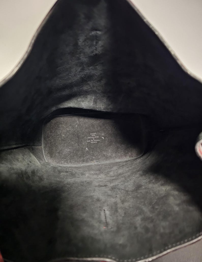 以下が含まれることがあります： 黒い革のトートバッグの内側。バッグは黒い布地で裏打ちされており、「イタリア製」と「本革」と書かれたラベルが付いています。