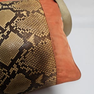 Peut inclure: Sac &agrave; bandouli&egrave;re avec un motif peau de serpent sur le devant, compl&eacute;t&eacute; par un panneau lat&eacute;ral en daim orange br&ucirc;l&eacute; et une bandouli&egrave;re beige. Le sac a une fermeture &eacute;clair et une forme rectangulaire.