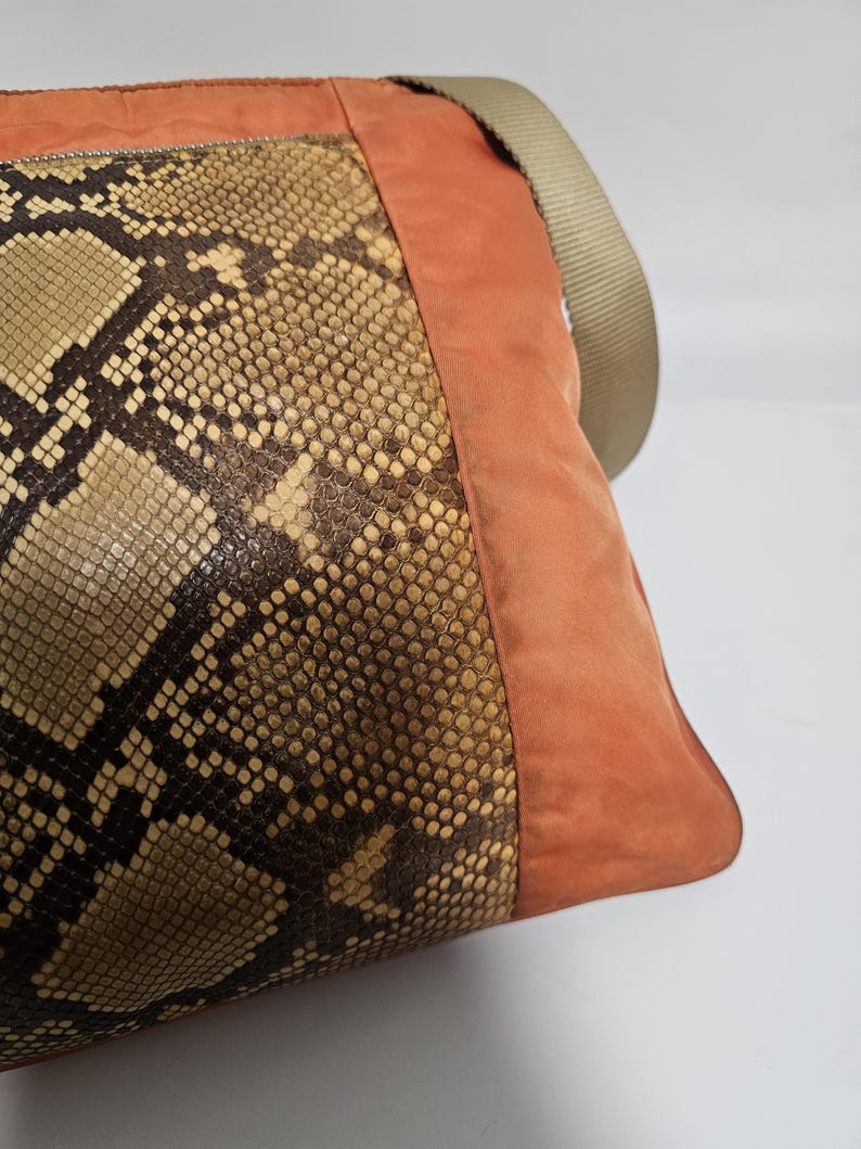 Peut inclure: Sac &agrave; bandouli&egrave;re avec un motif peau de serpent sur le devant, compl&eacute;t&eacute; par un panneau lat&eacute;ral en daim orange br&ucirc;l&eacute; et une bandouli&egrave;re beige. Le sac a une fermeture &eacute;clair et une forme rectangulaire.