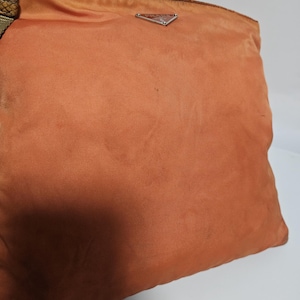 Peut inclure: Un sac &agrave; main orange avec un logo triangulaire argent&eacute;. Le sac a une bandouli&egrave;re en tissu avec un motif peau de serpent. Le sac est fait d'une mati&egrave;re douce, possiblement en nylon.
