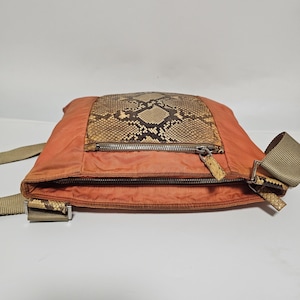 Peut inclure: Un sac bandouli&egrave;re orange avec un panneau en peau de serpent et une fermeture &eacute;clair. Le sac a une sangle beige et des accents en peau de serpent sur les attaches de la sangle. Le sac est en mati&egrave;re de type nylon.