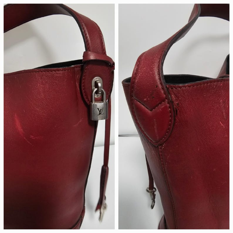 以下が含まれることがあります： 銀色の鍵と錠前が付いた赤い革のバケットバッグ。バッグはトップハンドルとショルダーストラップが付いています。