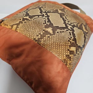 Peut inclure: Coussin carr&eacute; avec un panneau central en peau de serpent et une bordure en tissu couleur rouille. Le motif en peau de serpent pr&eacute;sente des nuances de marron, de beige et de cr&egrave;me. Une sangle verte est attach&eacute;e.