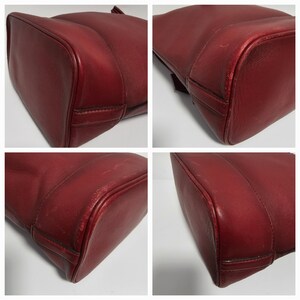 以下が含まれることがあります： 滑らかで質感のある赤い革製のトートバッグのクローズアップ。バッグは構造化された形状で、わずかに丸みを帯びた底をしています。