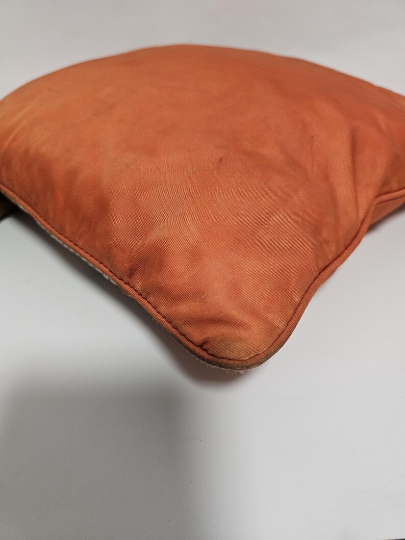 Peut inclure: Un coussin carr&eacute; orange avec un tissu textur&eacute;. Le coussin a une couture visible sur les bords et pr&eacute;sente des signes d'usure. La couleur est une teinte chaude et terreuse.