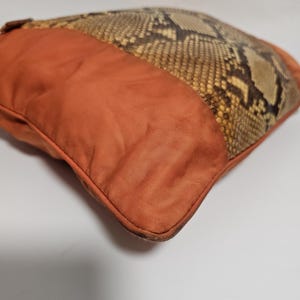 Peut inclure: Coussin carr&eacute; d&eacute;coratif avec un motif peau de serpent et un tissu orange uni. Le coussin a une bordure cousue et un aspect textur&eacute;. La section en peau de serpent est marron, beige et noire.