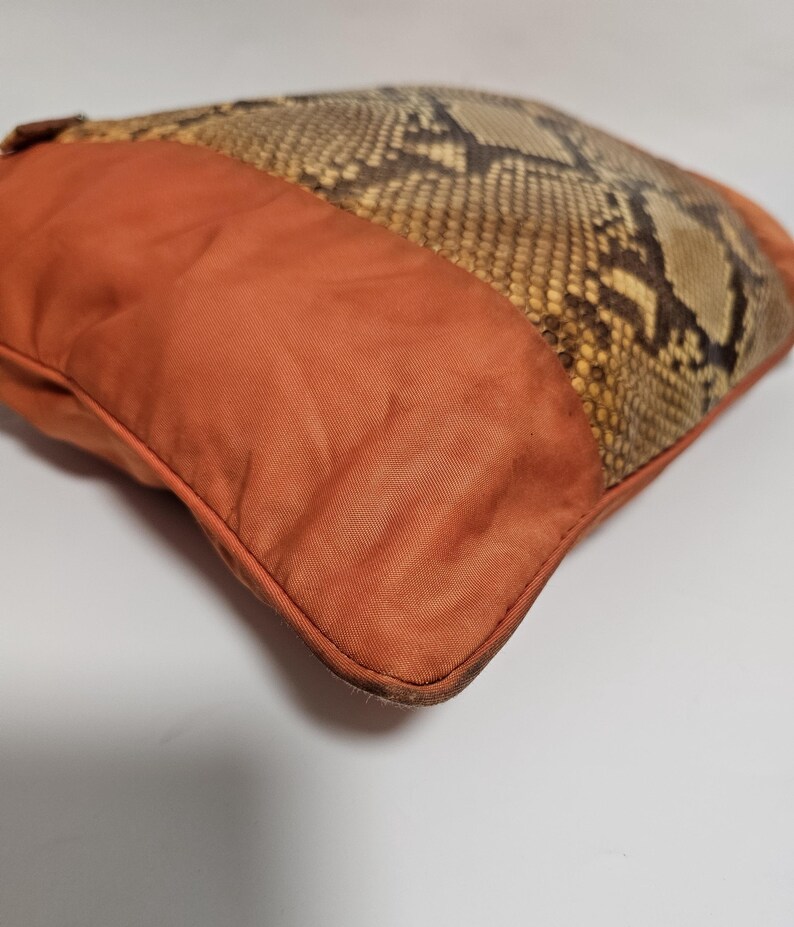 Peut inclure: Coussin carr&eacute; d&eacute;coratif avec un motif peau de serpent et un tissu orange uni. Le coussin a une bordure cousue et un aspect textur&eacute;. La section en peau de serpent est marron, beige et noire.