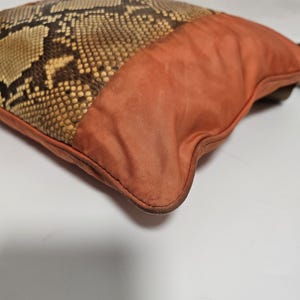 Peut inclure: Un coussin d&eacute;coratif avec un motif peau de serpent et un tissu orange uni. La section en peau de serpent pr&eacute;sente des tons marron, beige et cr&egrave;me, tandis que le tissu orange a une texture lisse. Le design du coussin est un m&eacute;lange d'&eacute;l&eacute;ments naturels et modernes.