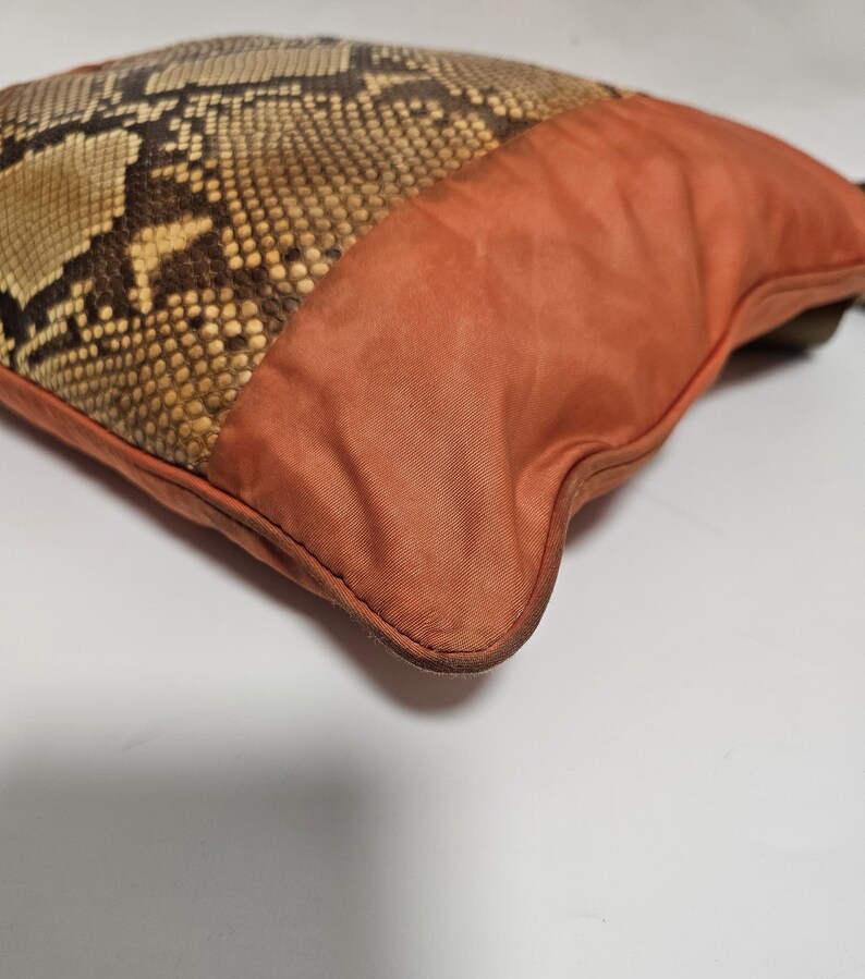 Peut inclure: Un coussin d&eacute;coratif avec un motif peau de serpent et un tissu orange uni. La section en peau de serpent pr&eacute;sente des tons marron, beige et cr&egrave;me, tandis que le tissu orange a une texture lisse. Le design du coussin est un m&eacute;lange d'&eacute;l&eacute;ments naturels et modernes.