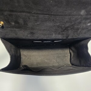 K&ouml;nnte beinhalten: Offene Ansicht des Inneren einer schwarzen Handtasche. Das Innere der Tasche ist mit schwarzem Stoff gef&uuml;ttert und hat eine kleine Tasche. Die Klappe der Tasche ist ge&ouml;ffnet und gibt den Blick ins Innere frei. Ein goldfarbener Verschluss ist sichtbar.