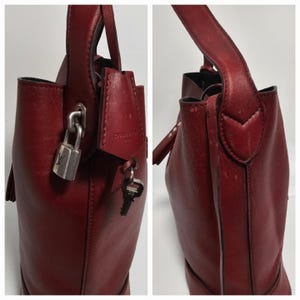 以下が含まれることがあります： 鍵とキーが付いたワインレッドの革製のハンドバッグ。バッグはトップハンドルとタッセルが付いています。