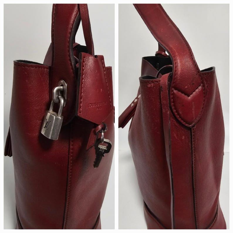 以下が含まれることがあります： 鍵とキーが付いたワインレッドの革製のハンドバッグ。バッグはトップハンドルとタッセルが付いています。