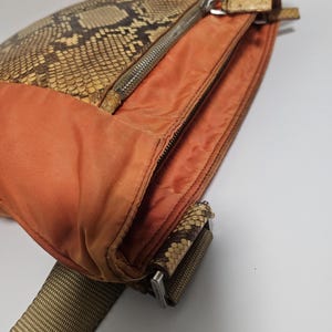 Peut inclure: Un sac bandouli&egrave;re orange avec un rabat en peau de serpent et une fermeture &eacute;clair argent&eacute;e. Le sac est dot&eacute; d'une bandouli&egrave;re tiss&eacute;e marron et beige. Le sac est fait de cuir et de tissu.