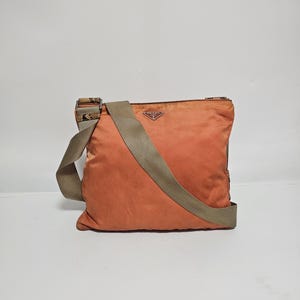 Peut inclure: Sac bandouli&egrave;re Prada orange avec une bandouli&egrave;re beige. Le sac est de forme carr&eacute;e et porte un petit logo Prada. La bandouli&egrave;re pr&eacute;sente un motif sur les extr&eacute;mit&eacute;s.