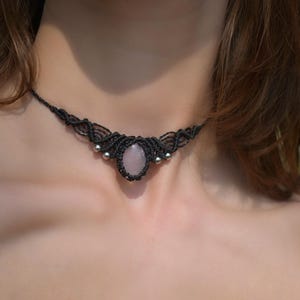 May include: Black macrame choker necklace with a central oval rose quartz stone and small silver beads. The necklace is worn around the neck and is a handmade piece of jewelry.
