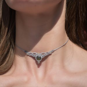 Peut inclure: Un collier macramé gris fait à la main, orné d'une pierre verte foncée en son centre. Le collier, de style ras-du-cou, est orné de petites perles dorées et présente un design délicat.
