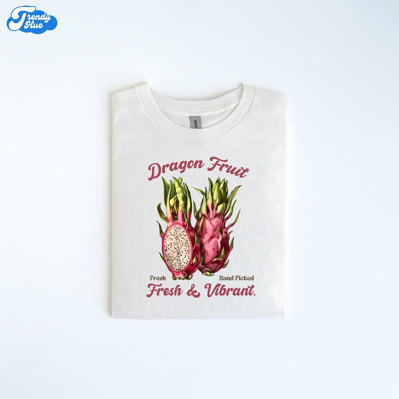May include: White t-shirt with a dragon fruit design. The graphic shows two dragon fruits, one sliced open, in pink and green hues. Text reads "Dragon Fruit" and "Fresh & Vibrant". The t-shirt is made of a soft material.