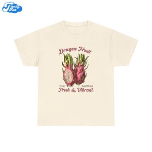May include: A cream-coloured t-shirt with a vintage illustration of dragon fruit. The design includes the text "Dragon Fruit," "Fresh," "Hand Picked," and "Fresh & Vibrant." The dragon fruit is shown in pink, green, and white.